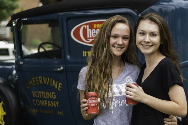 Two girls posing with cheerwine and antique car